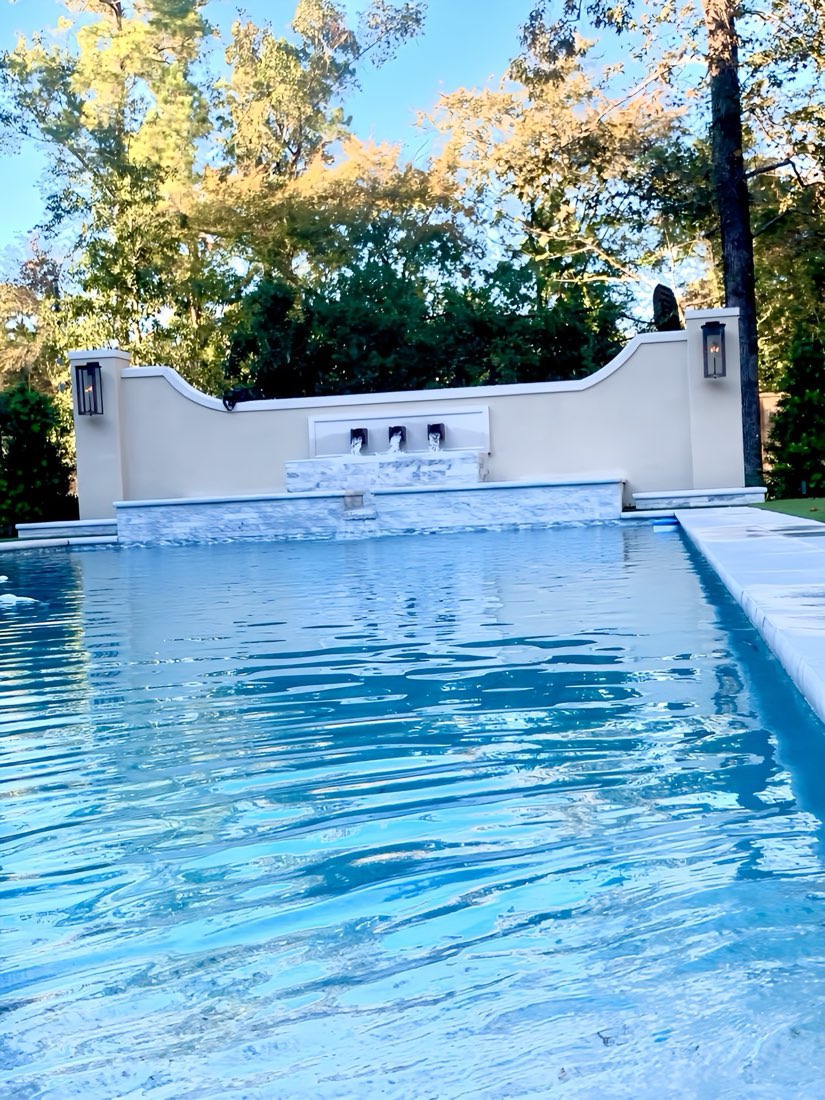 Sparkling clean pool with fountain wall maintained by Suns Out Buns Out Pools in Spring TX